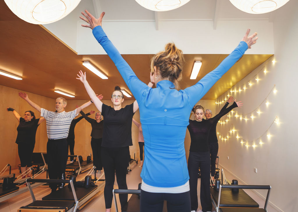 Instructor leading a standing class with arms reaching overhead